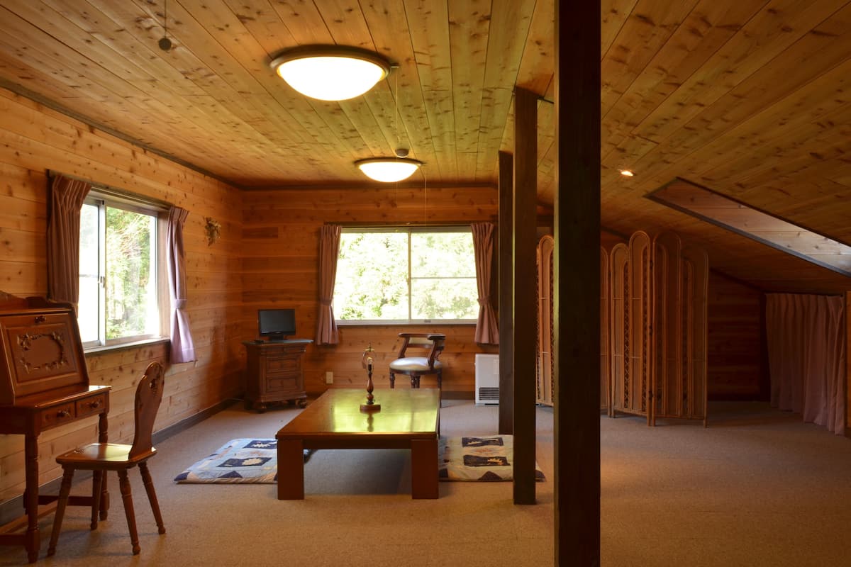 A log cabin interior with a wooden table, chairs, a television, and a large window.
