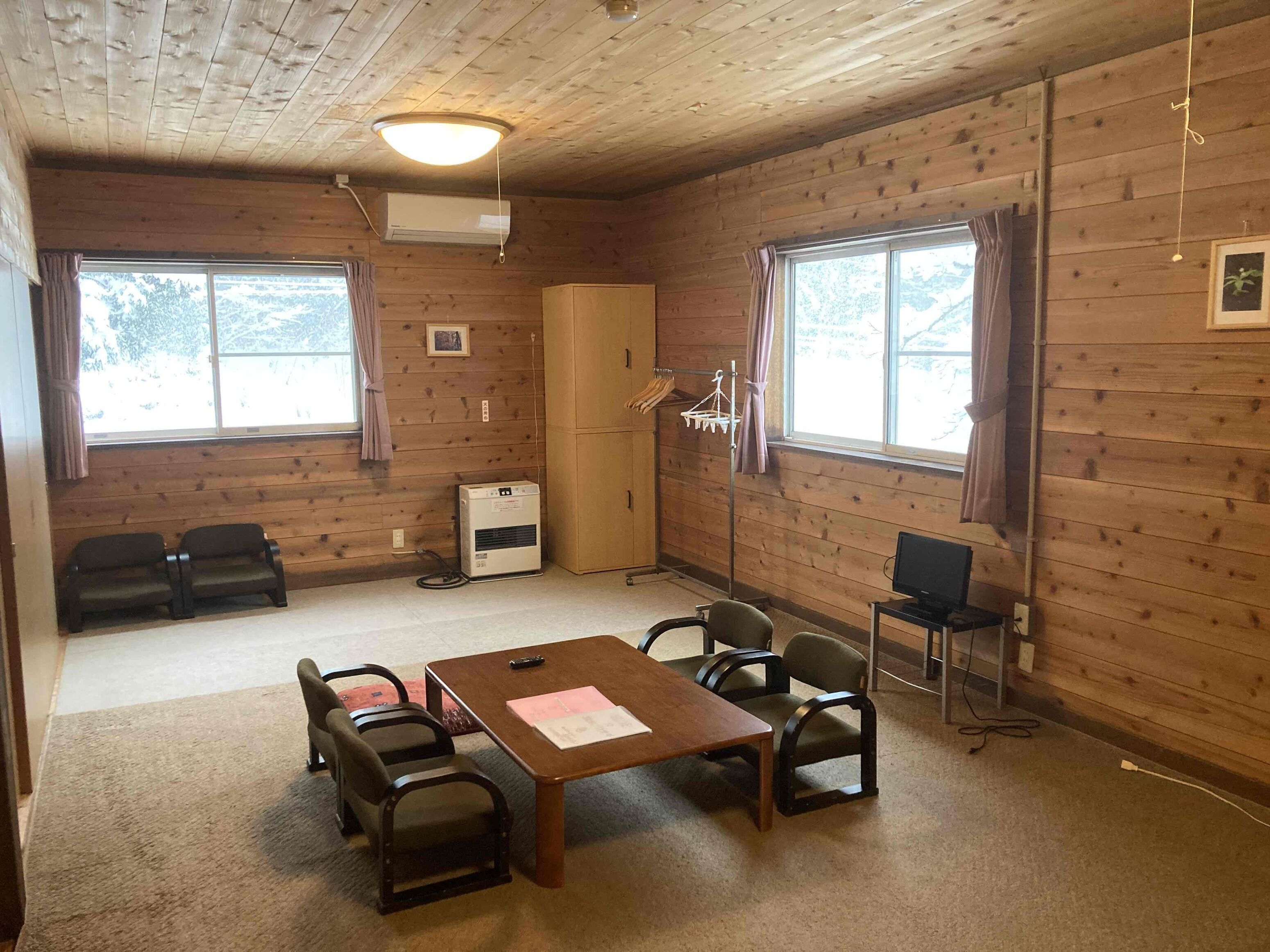 Una habitación con paredes de madera, una mesa con sillas, un televisor, un equipo de aire acondicionado y una ventana con cortinas.