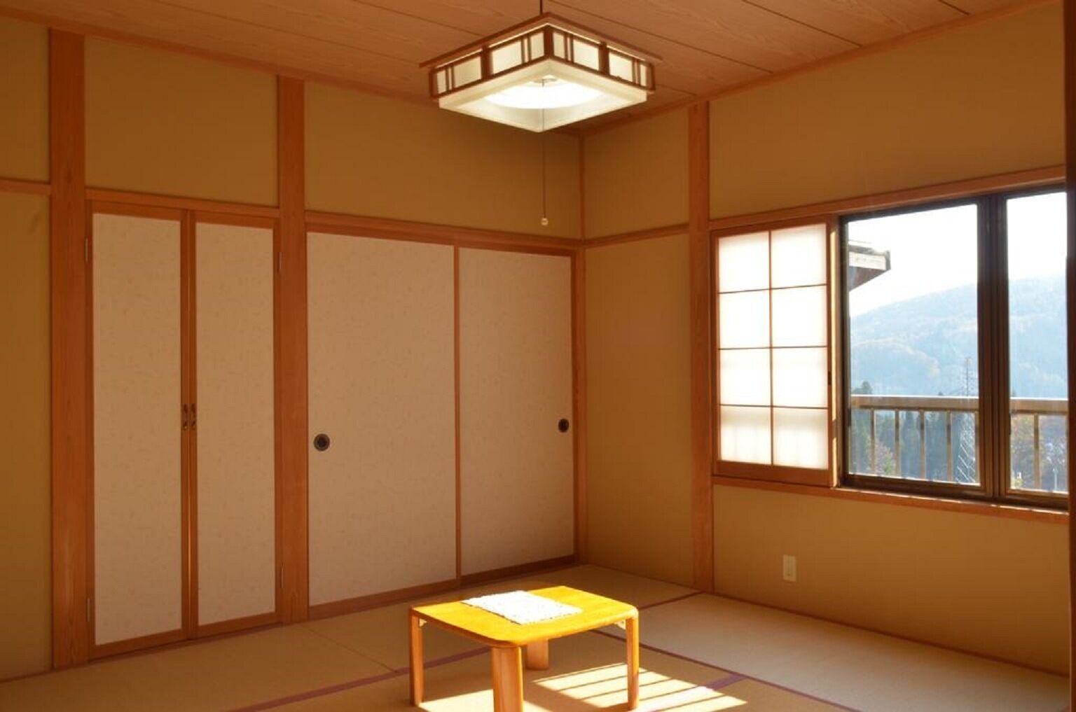 Una habitación japonesa tradicional con suelo de tatami, puertas correderas, una mesita y una ventana con vistas.