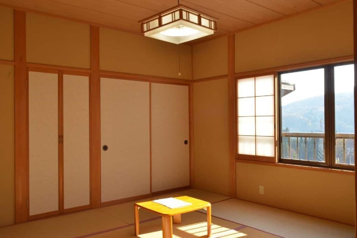 A traditional Japanese room with tatami flooring, sliding doors, a small table, and a window with a view.