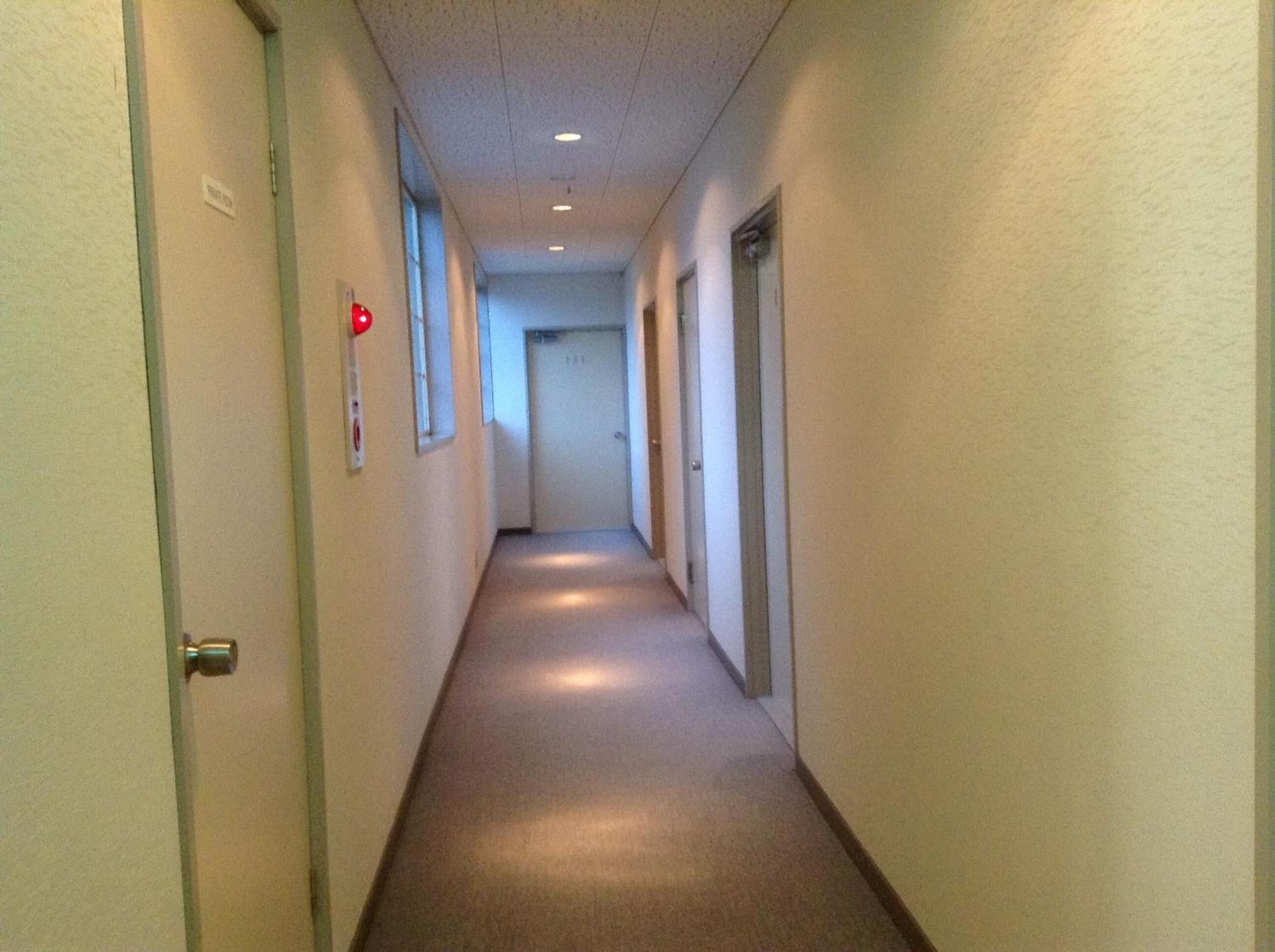 A narrow, well-lit hallway with doors on both sides, leading to individual rooms.