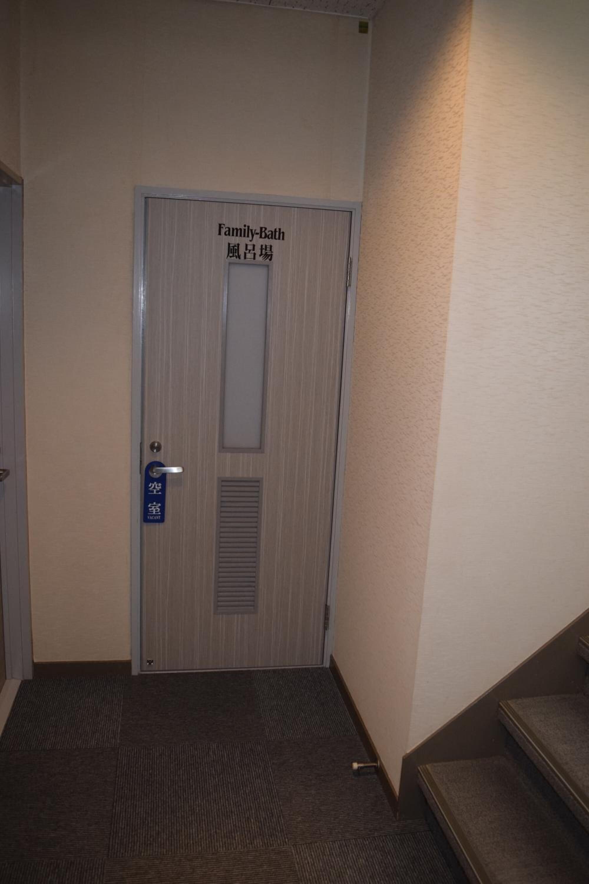 Puerta de baño familiar con panel de ventilación y un letrero azul que indica habitación accesible para sillas de ruedas.