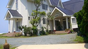 A large, two-story house with a steeply pitched roof, multiple windows, and a covered front porch. - Seaside Resort Pension Surfrider (Nishiizu)