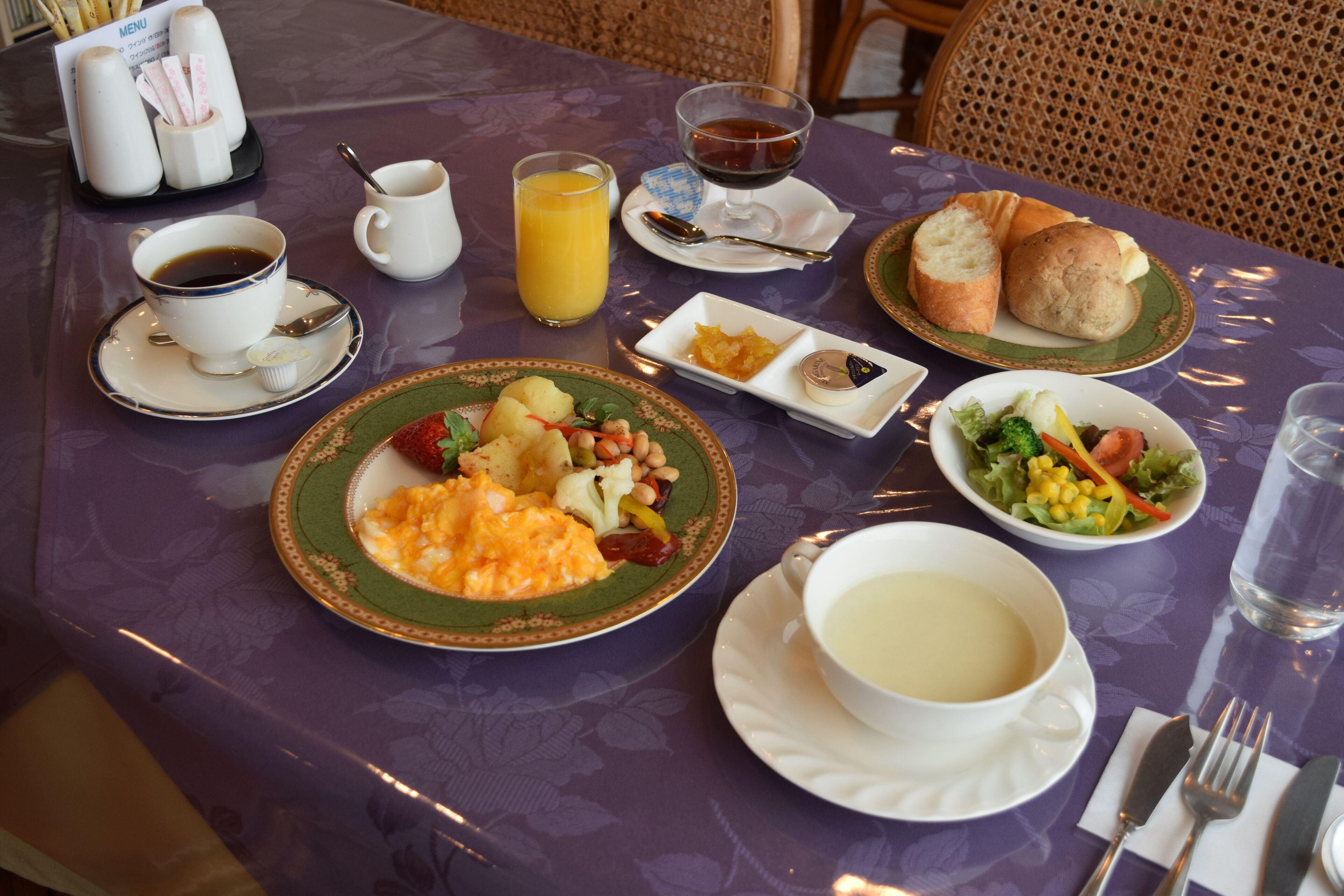 A table set with breakfast items including eggs, toast, soup, and a fruit bowl.