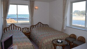 A hotel room with two beds, a desk, and a view of the beach. - Seaside Resort Pension Surfrider (Nishiizu)