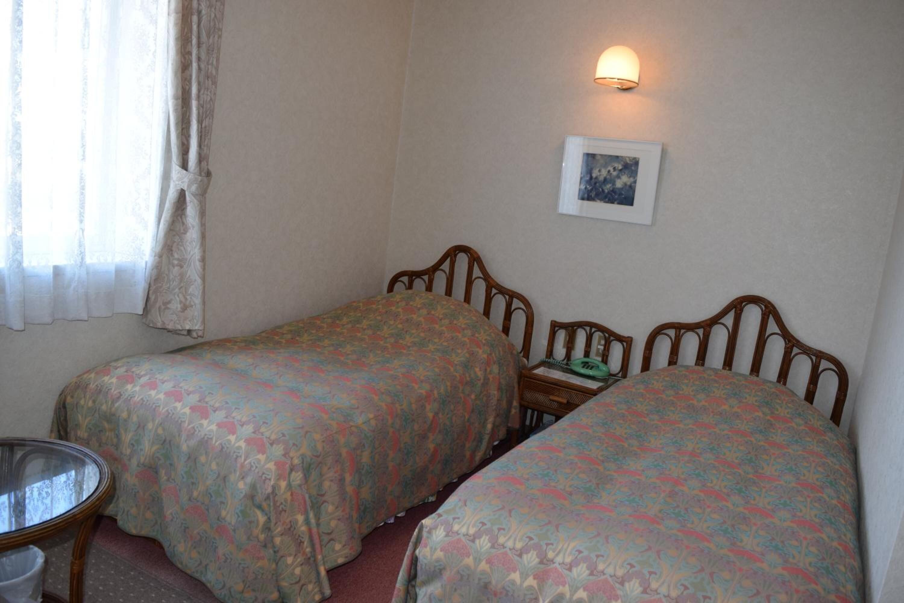 Una habitación con dos camas individuales, una mesita, una silla y una lámpara fijada a la pared.