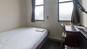 A small, single-bed room with a desk and chair, two windows with curtains, and a visible power outlet.