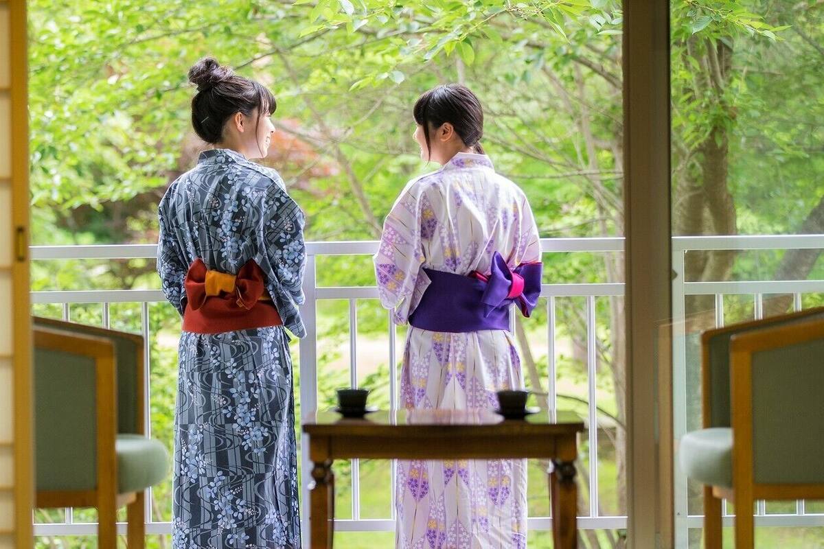 Two individuals in traditional attire standing by a window with a view of greenery.