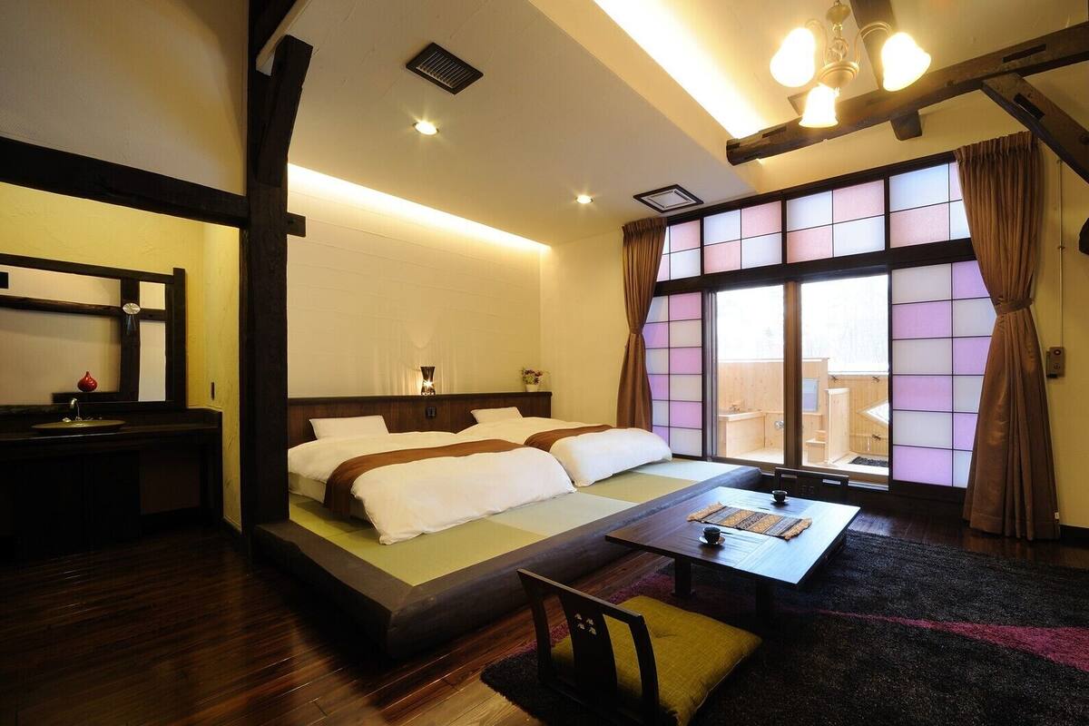 A hotel room with a bed, a small table, a TV, and a window with curtains.