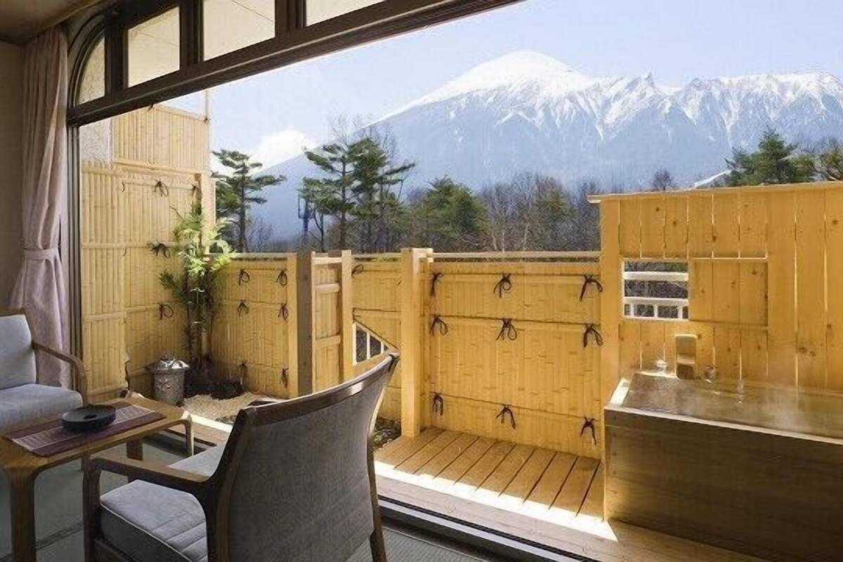 A balcony with a view of snow-capped mountains, wooden furniture, and a small table.