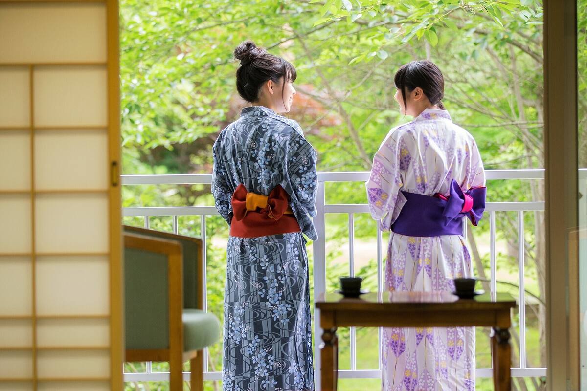 Two individuals in traditional attire standing on a balcony with a view of a forest.