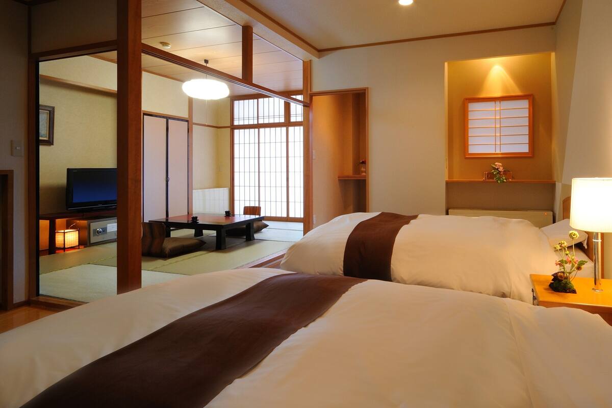 A hotel room with a bed, a television, a desk with a lamp, and a window with a view.