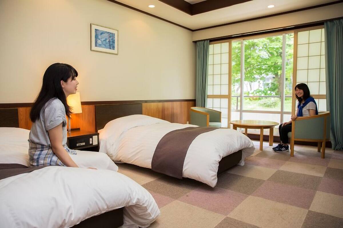 A hotel room with two beds, a small table, and a window with curtains.