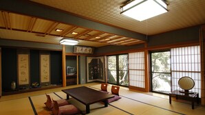 A tatami mat room with a low table, cushions, a television, and sliding doors. - Nisshinkan (Kusatsu)