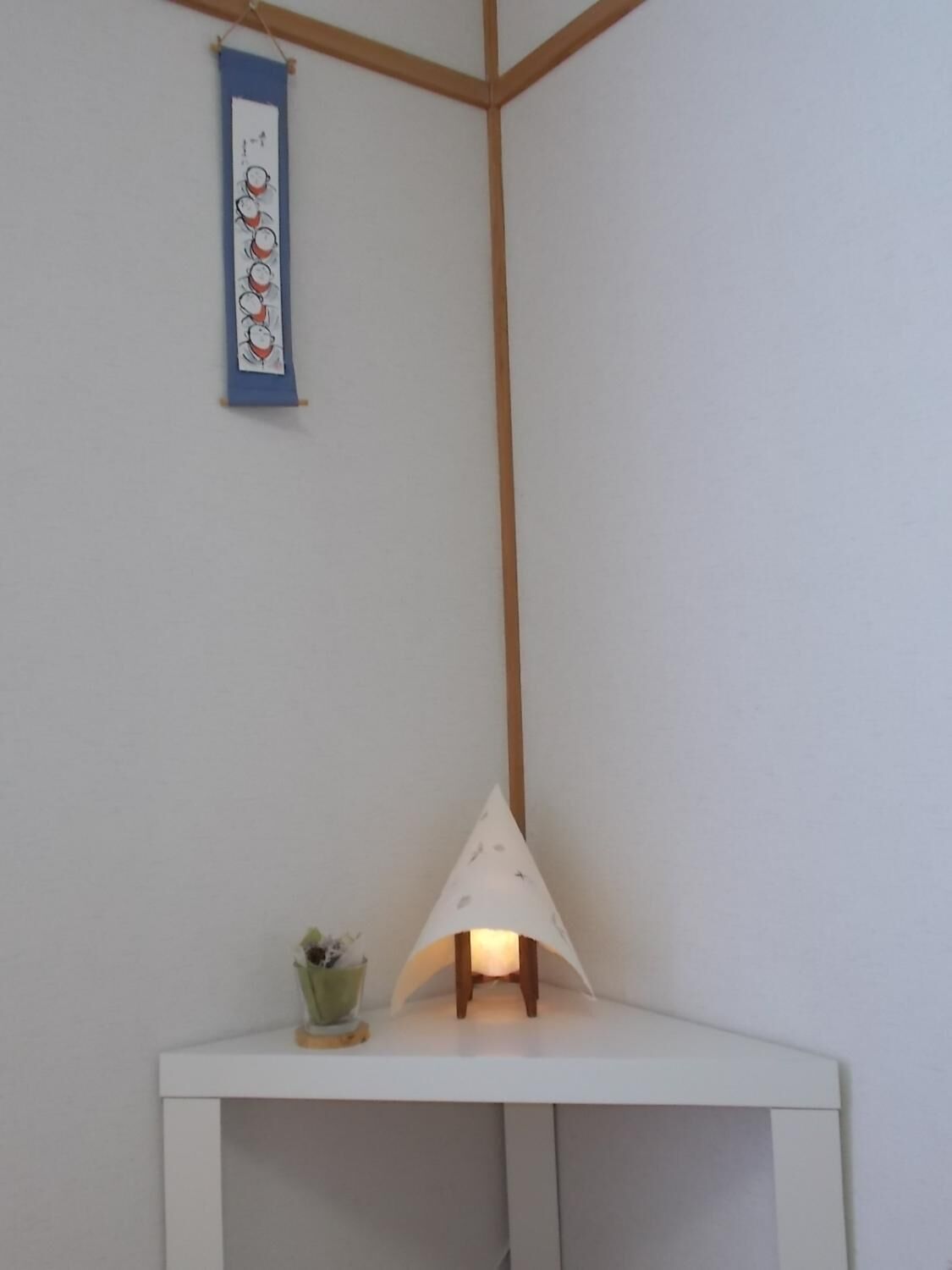 A corner of a room with a white table, a small green plant, and a hanging wall decoration.