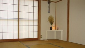 Una stanza con tatami, un paravento shoji, un tavolino con un vaso e un decoro appeso.