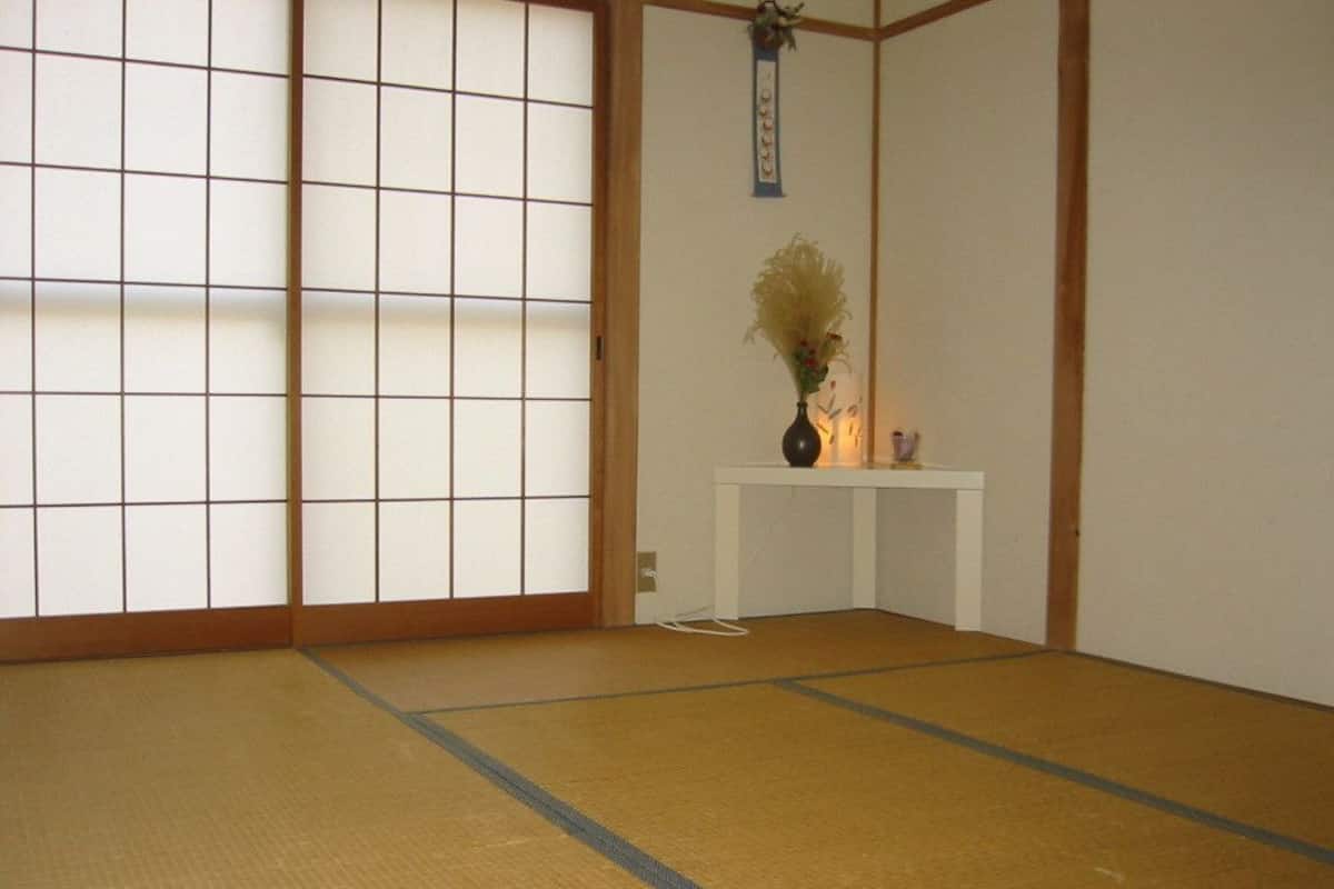 A tatami mat room with a shoji screen, a small table with a vase, and a hanging decoration.
