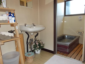 A bathroom with a sink, a small trash bin, a wooden shelf with toiletries, and a bathtub.