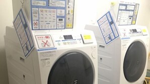 Two white front-loading washing machines with control panels, placed on a tiled floor in a room. - Smile Hotel Nagoya Shinkansenguchi (Nagoya)
