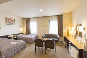 Ett hotellrum med två sängar, ett skrivbord med en stol, en lampa och ett litet kylskåp.