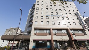 Ein mehrstöckiges Hotel mit modernem Design, das durch einen markanten Eingangsbereich mit blauer Markise und ein Schild, das es als Park Side Hotel in Takamatsu kennzeichnet, gekennzeichnet ist.