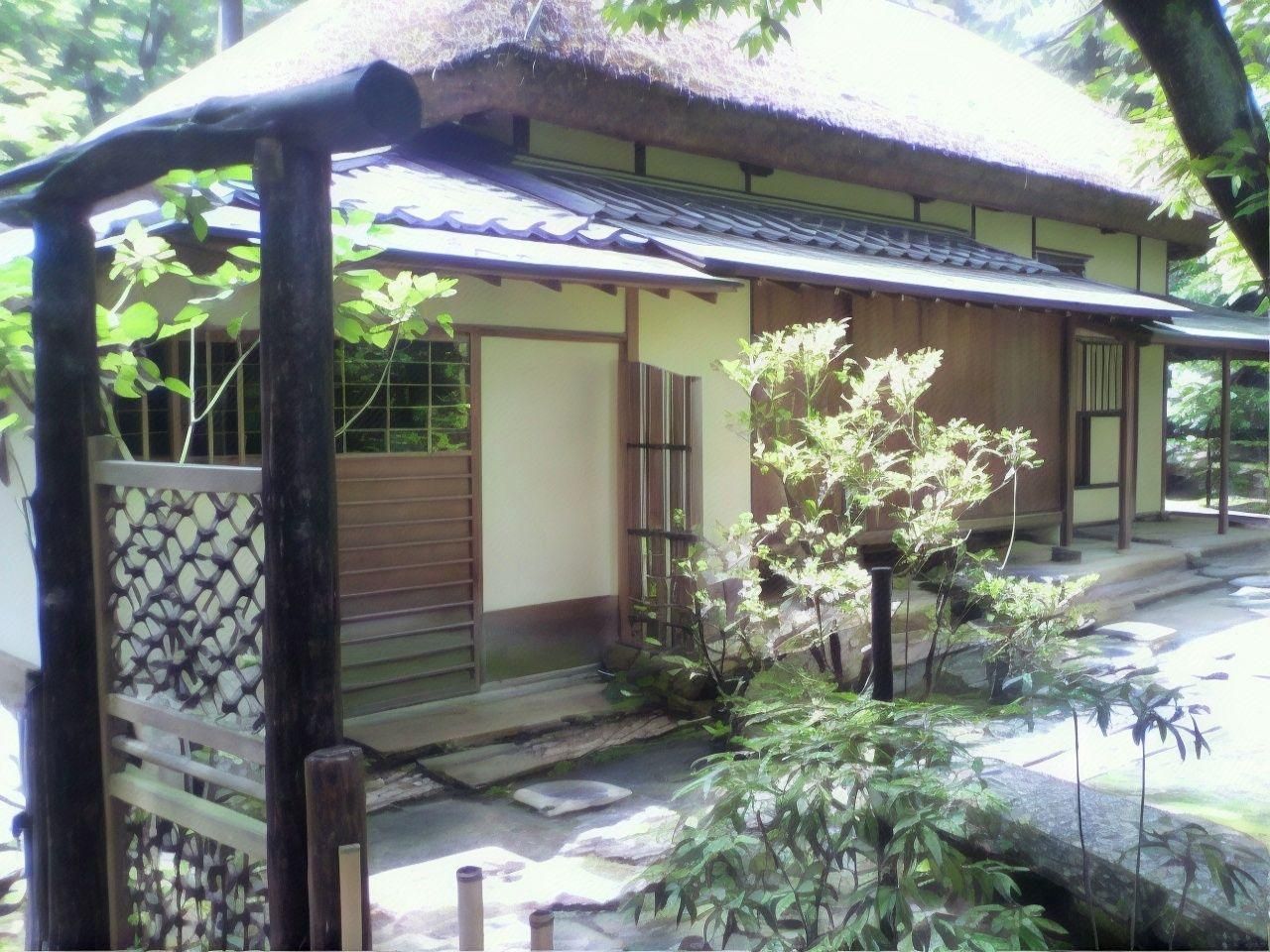 A traditional Japanese building with a thatched roof, wooden doors, and a small garden area with plants and a stone pathway.