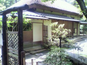 A traditional Japanese building with a thatched roof, wooden doors, and a small garden area with plants and a stone pathway. - Business Hotel Park Side Takamatsu (Takamatsu)