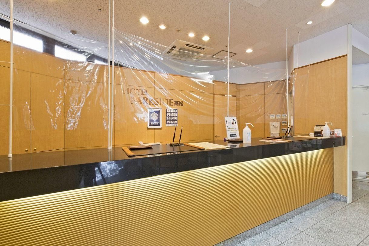 Zona de recepción de un hotel con un mostrador de madera, una barra negra y un cartel con el nombre del hotel.