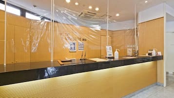 Zona de recepción de un hotel con un mostrador de madera, una barra negra y un cartel con el nombre del hotel.
