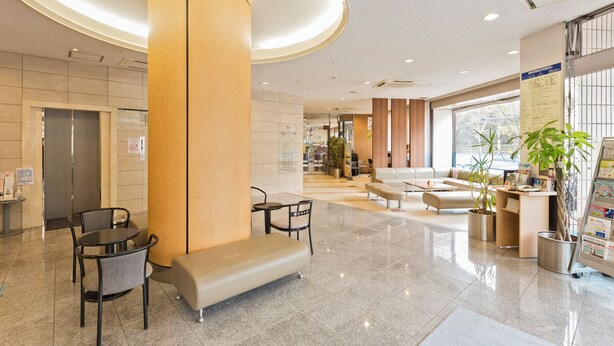 Eine moderne Lobby mit einer großen Säule, einer Sitzecke und einem Empfangstresen mit Pflanzen.