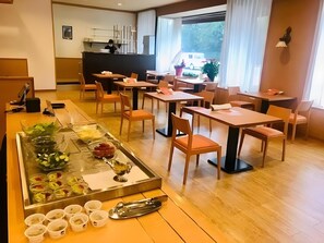 A restaurant with wooden tables and chairs, a buffet area with various food items, and a view of the outdoors through large windows. - Business Hotel Park Side Takamatsu (Takamatsu)