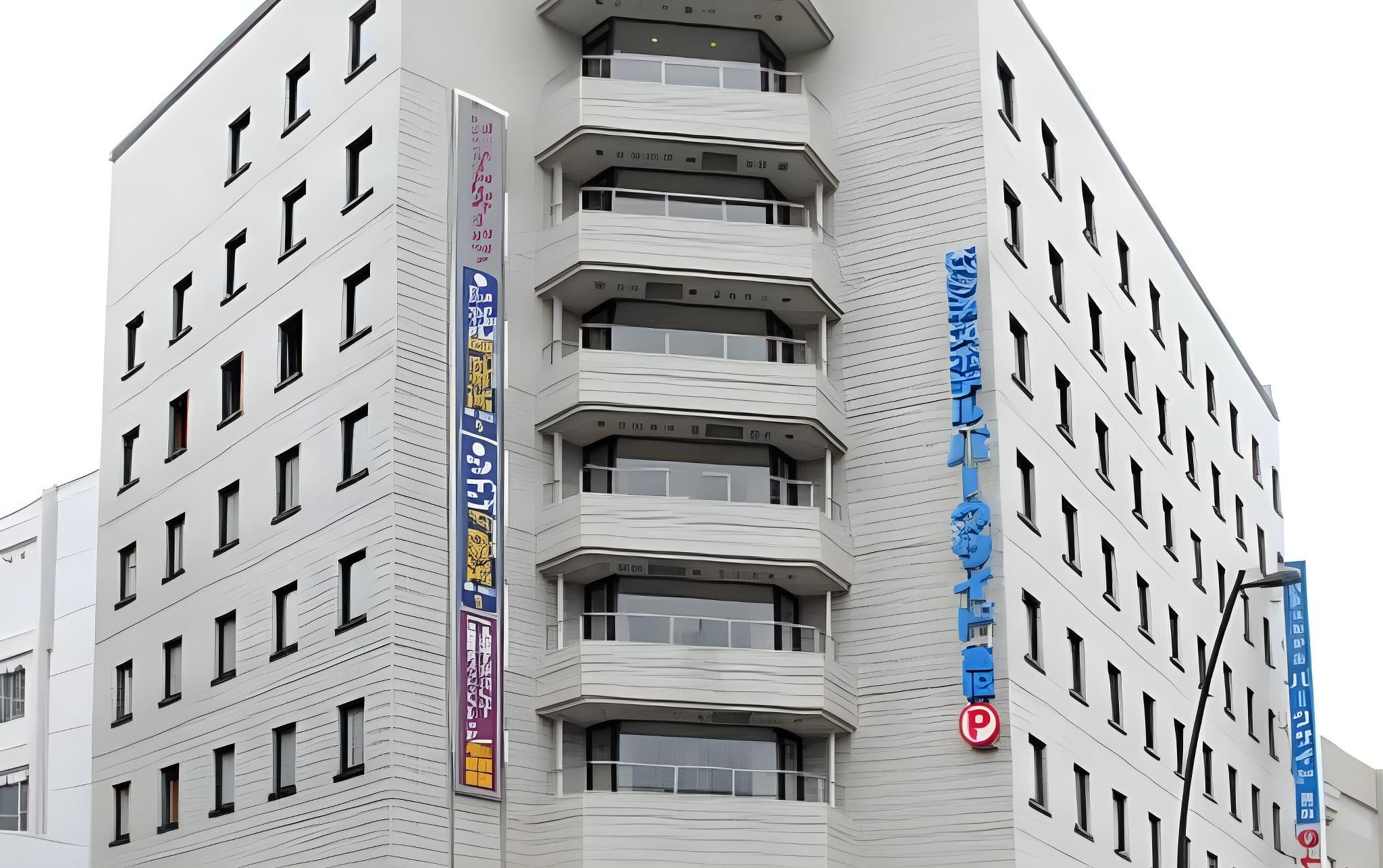 A multi-story building with a modern architectural design, featuring balconies and a prominent vertical sign with text.
