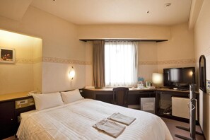 Ett hotellrum med en säng, ett skrivbord med en dator, en tv och ett badrum.