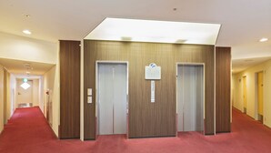 Ein Hotelkorridor mit rotem Teppich, Holzwandverkleidung und zwei Aufzügen.