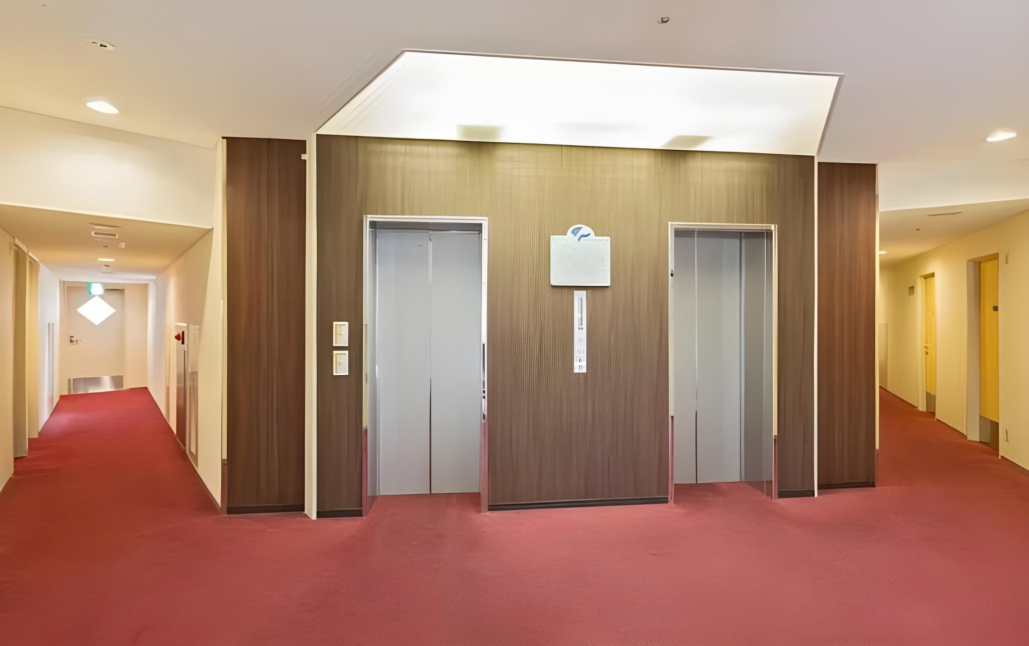 A hotel hallway with a red carpet, wooden panel walls, and two doors.