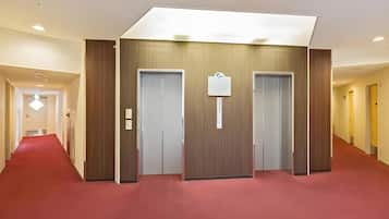 A hotel hallway with a red carpet, wooden panel walls, and two doors.