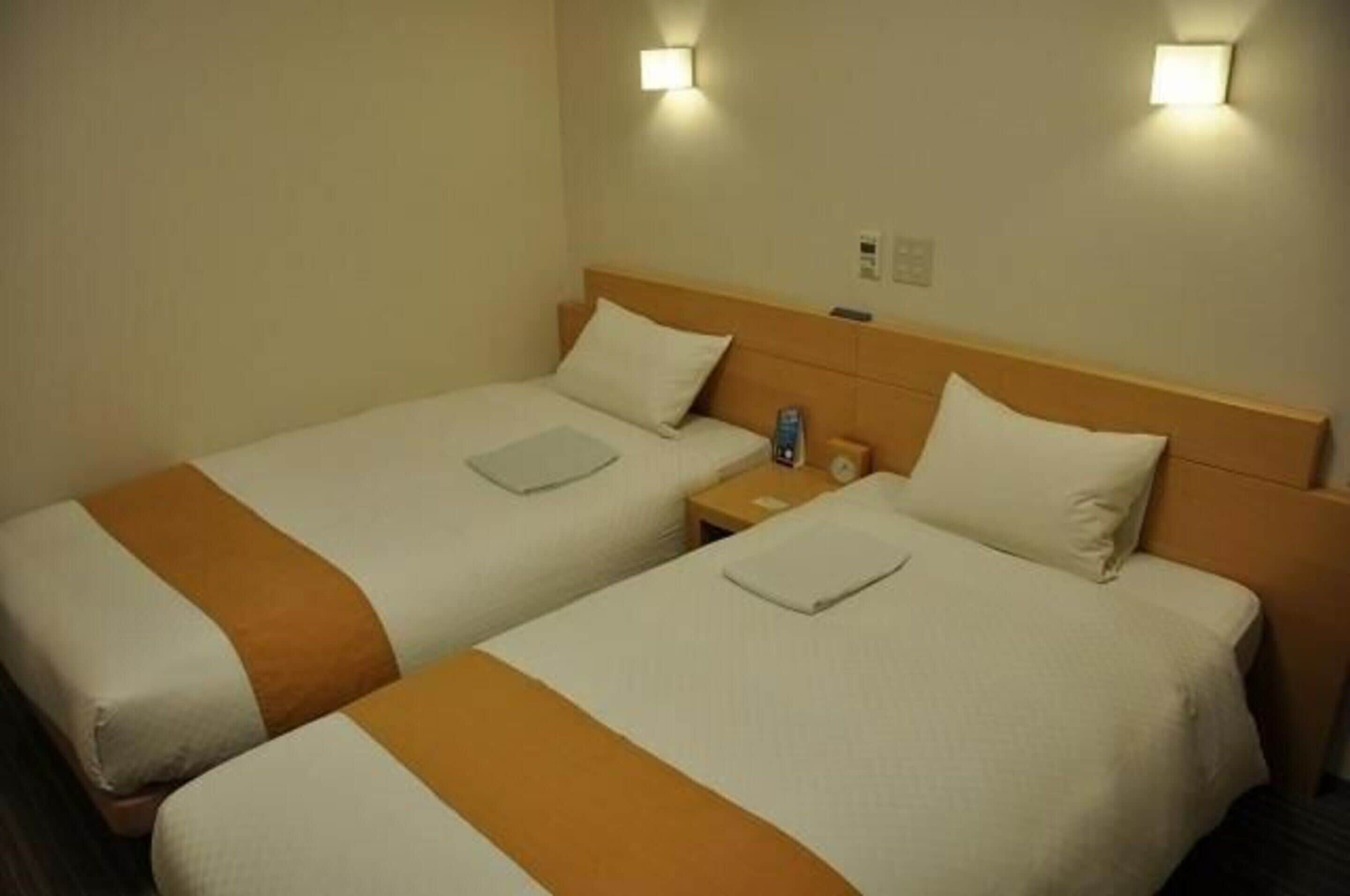 A hotel room with two single beds, each with a headboard, bedside tables, and a nightstand.