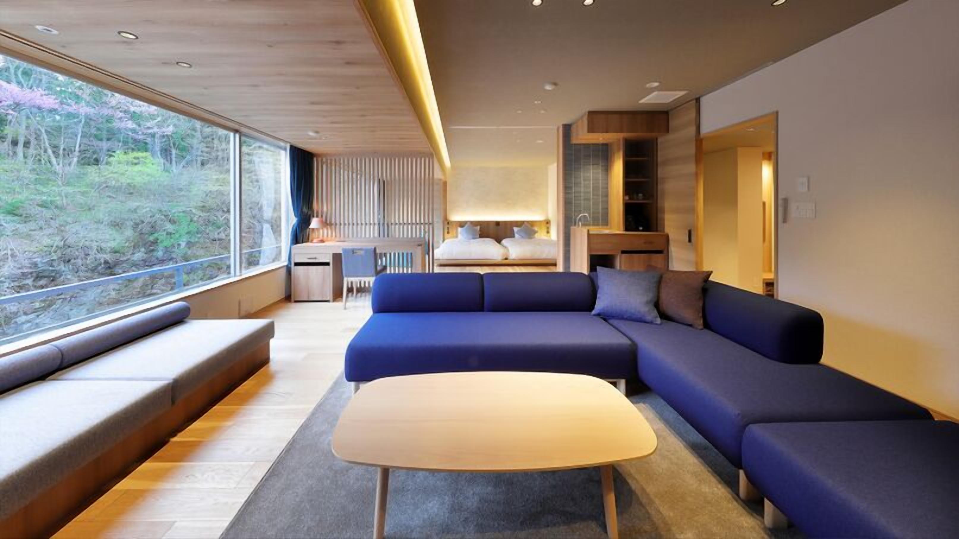 Een moderne woonkamer met een grote modulaire bank, een bijzettafeltje en uitzicht op de omgeving door grote ramen.