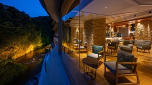 A modern interior with a stone wall, wooden furniture, and a view of a river at dusk. - Yu No Mori Hotel Shidotaira (Hanamaki)