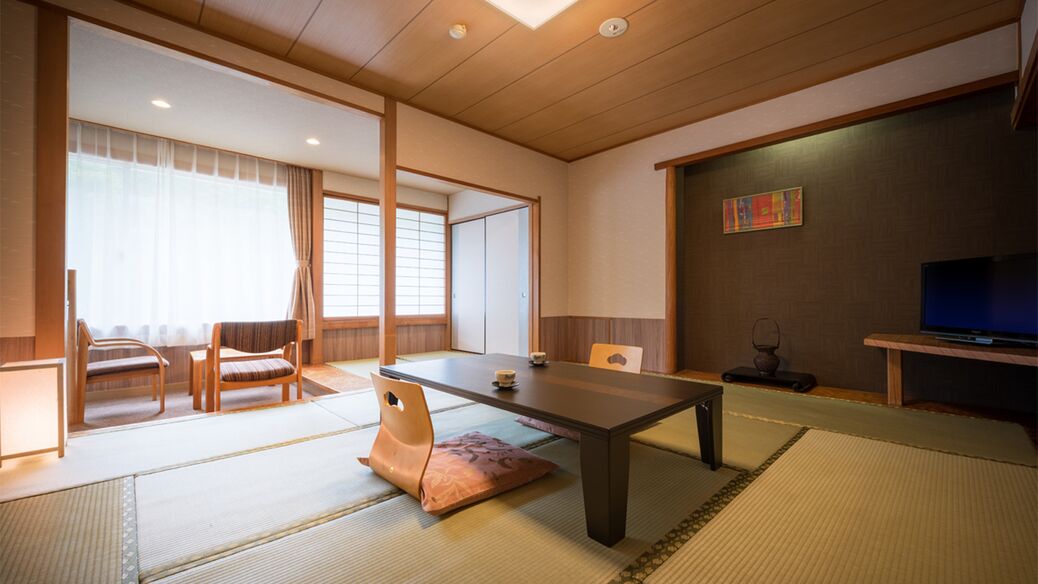 Une pièce de style japonais traditionnel, avec un sol recouvert de tatamis, une table basse, des chaises, un téléviseur et des portes coulissantes.