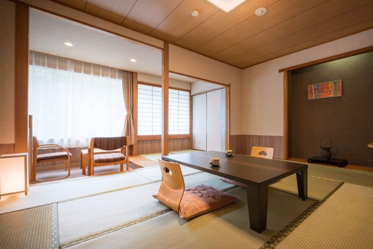 Ett traditionellt japanskt rum med tatamimattor på golvet, ett lågt bord, stolar, en tv och skjutdörrar.