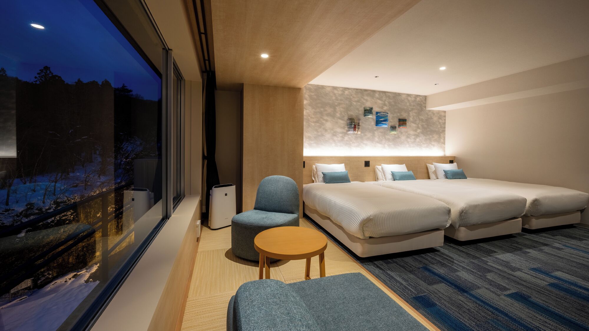 Een moderne hotelkamer met een groot raam, twee bedden, een tafeltje en een stoel.