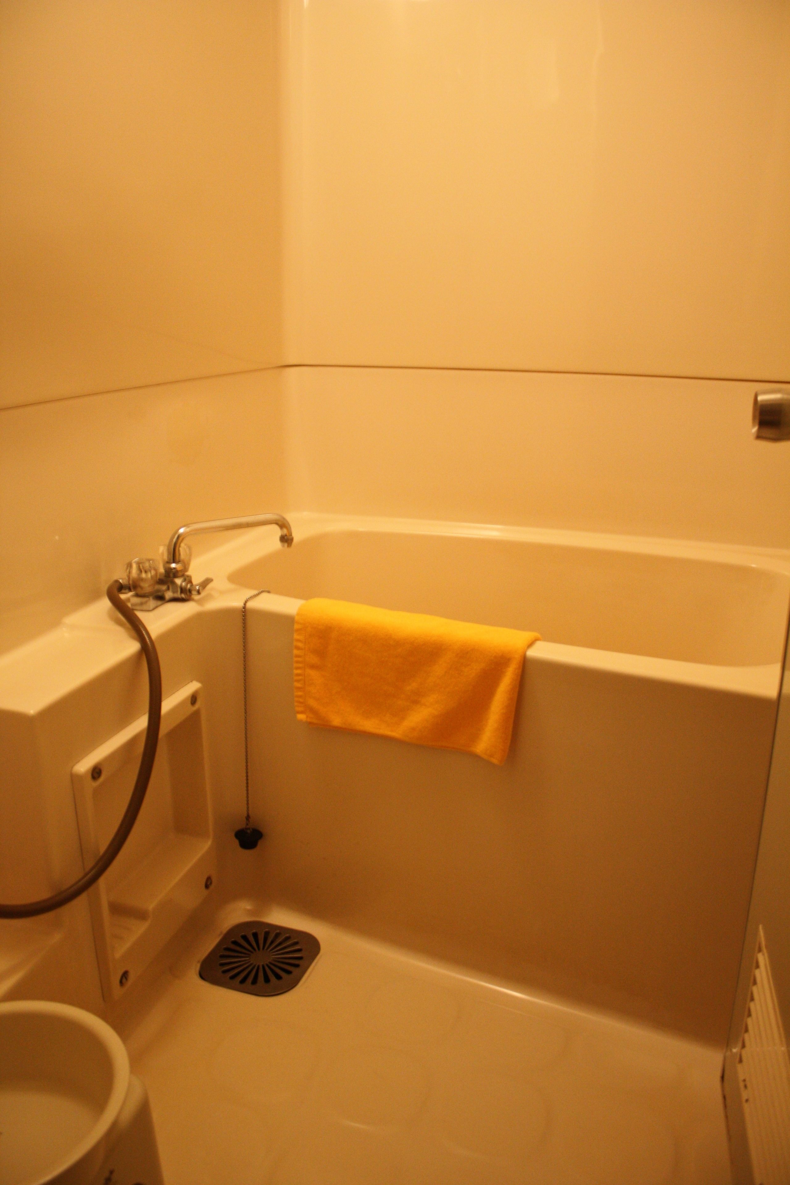 A bathroom with a bathtub, a yellow towel hanging on the side, a showerhead, and a drain.