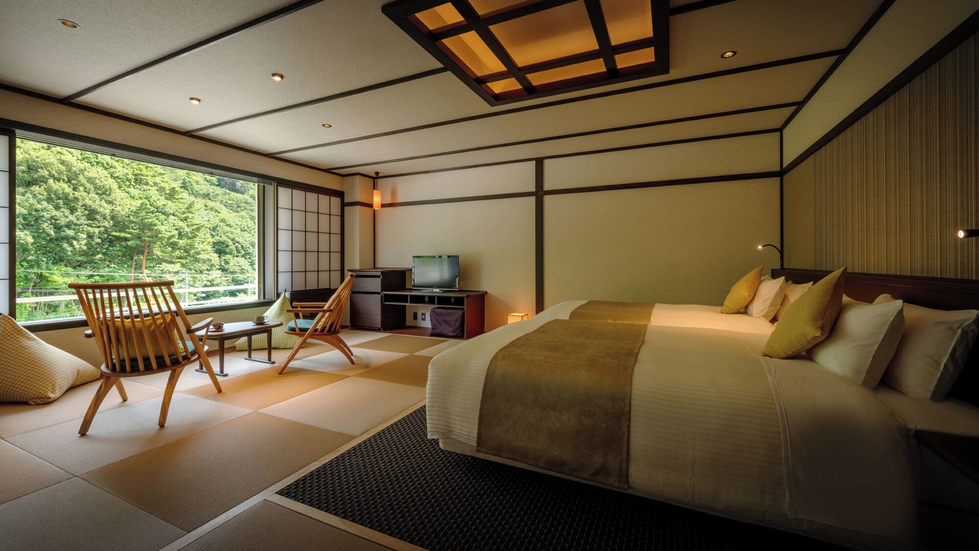 Een moderne hotelkamer met een groot bed, een televisie, een zithoek met stoelen en uitzicht op groen.