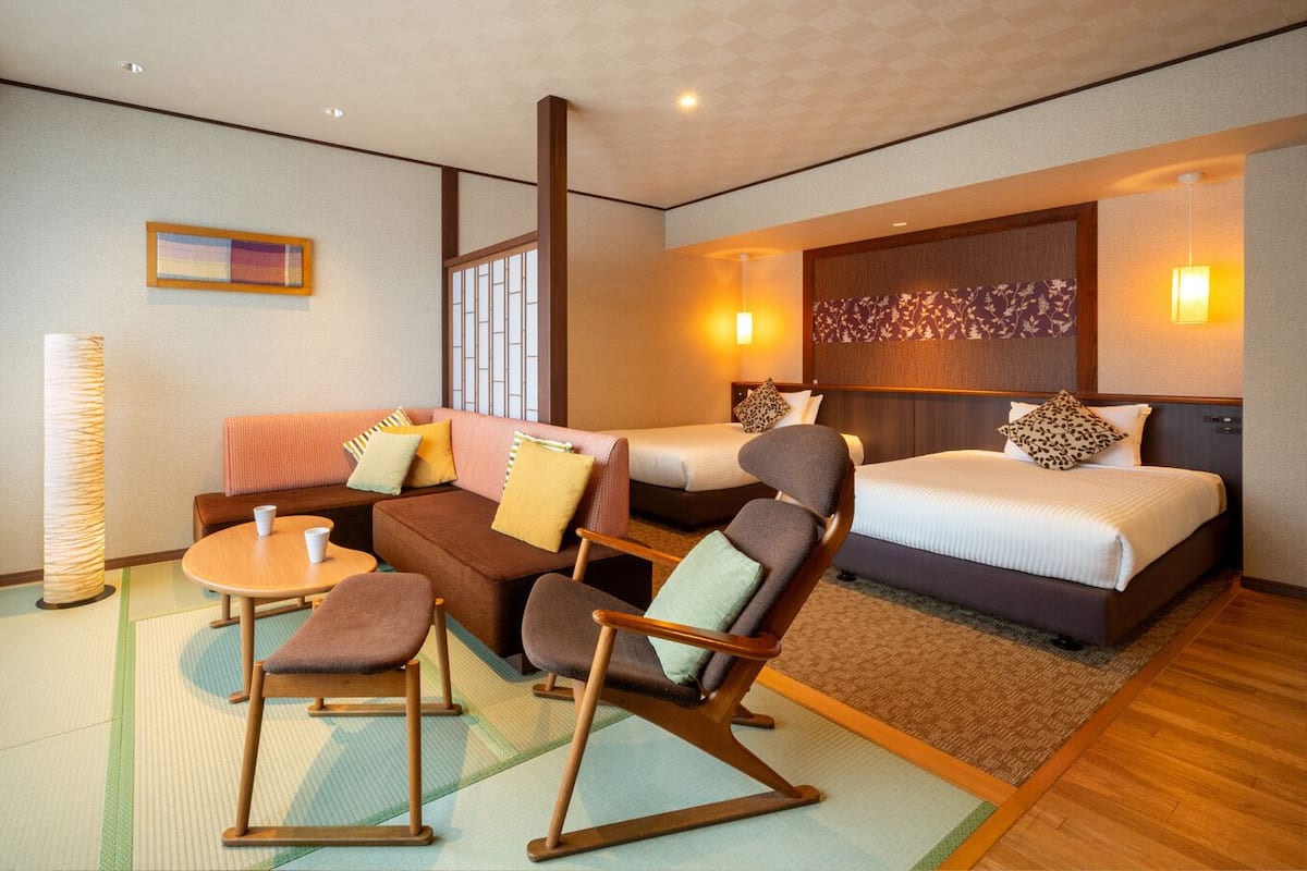 Ett hotellrum med en soffa, stolar, ett litet bord, en säng och ett stort fönster.