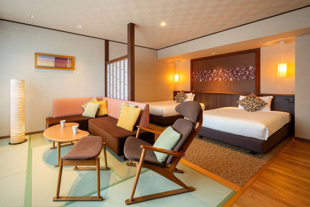 Une chambre d’hôtel avec un canapé, des fauteuils, une petite table, un lit et une grande fenêtre.
