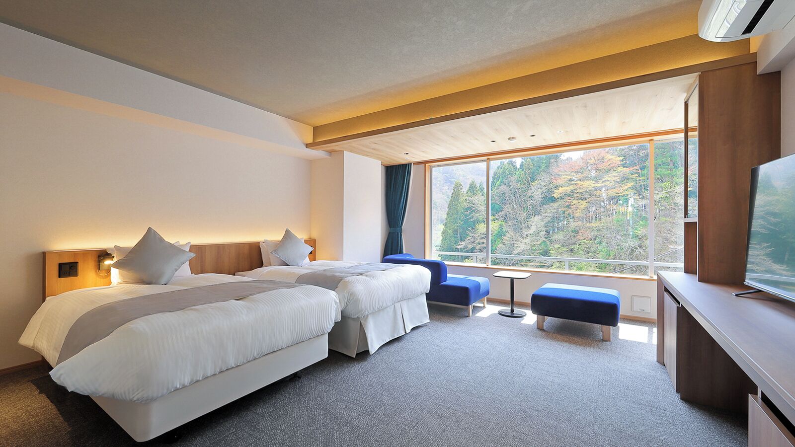 Een hotelkamer met twee bedden, een bureau, een televisie en een groot raam met uitzicht op bomen.