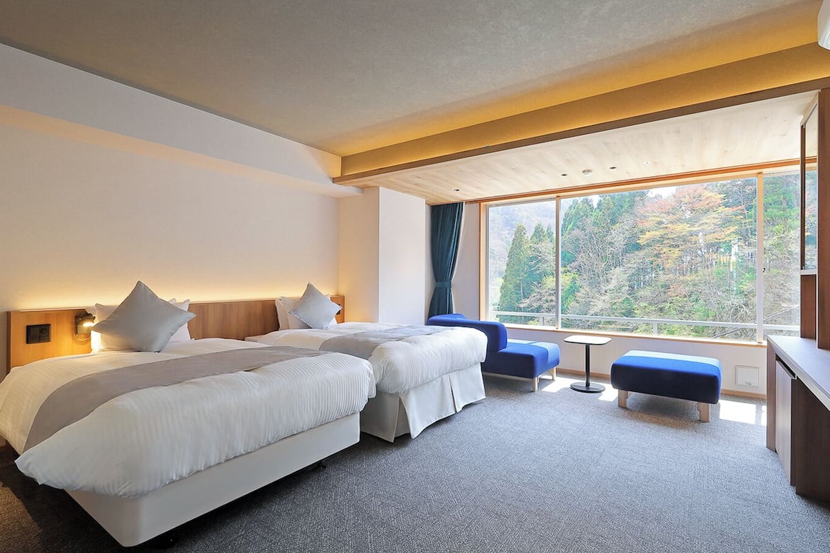 Ett hotellrum med två sängar, ett skrivbord, en TV och ett stort fönster med utsikt över träd.