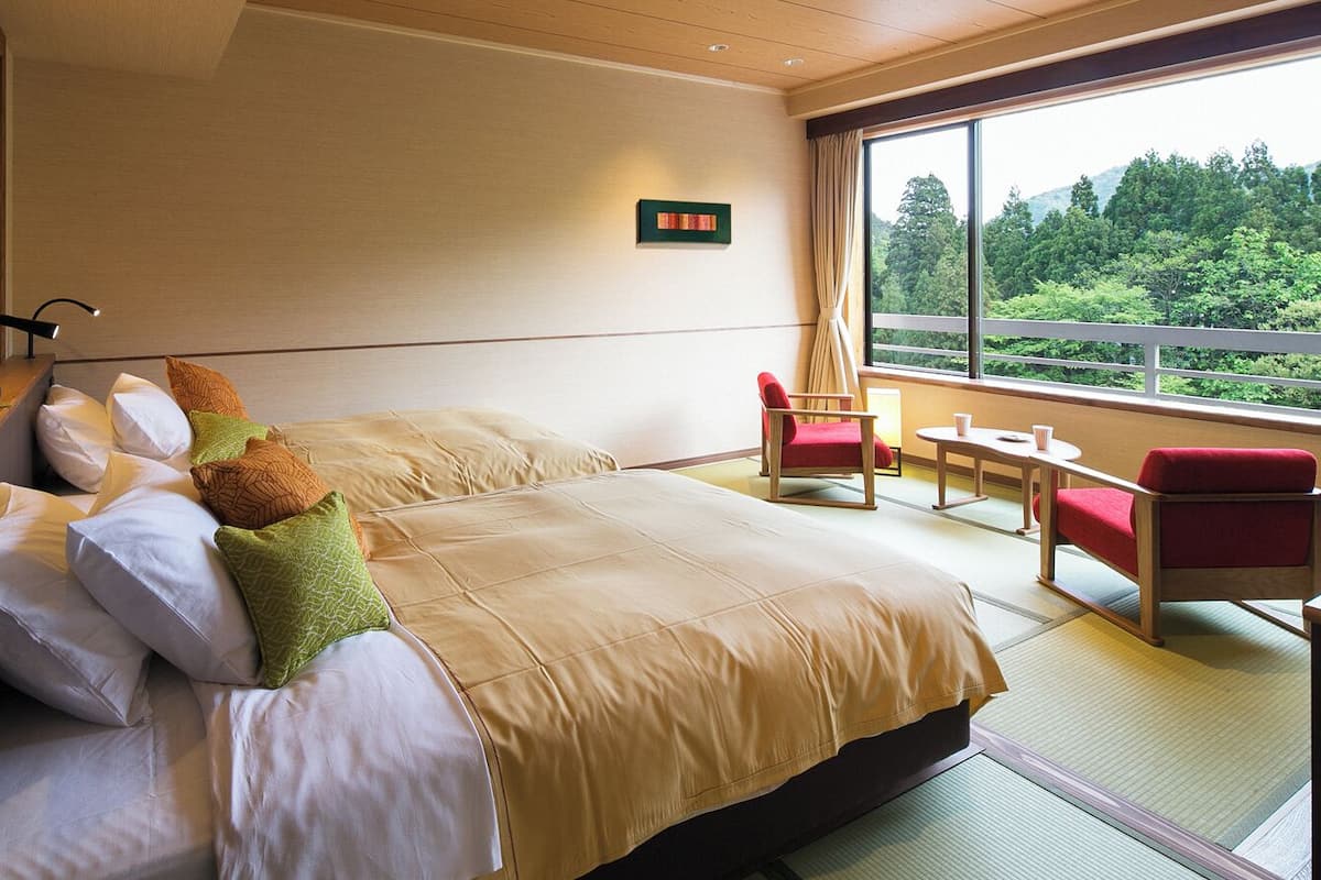 Ett hotellrum med en stor säng, ett litet bord, två stolar och utsikt över grönområden genom fönstret.