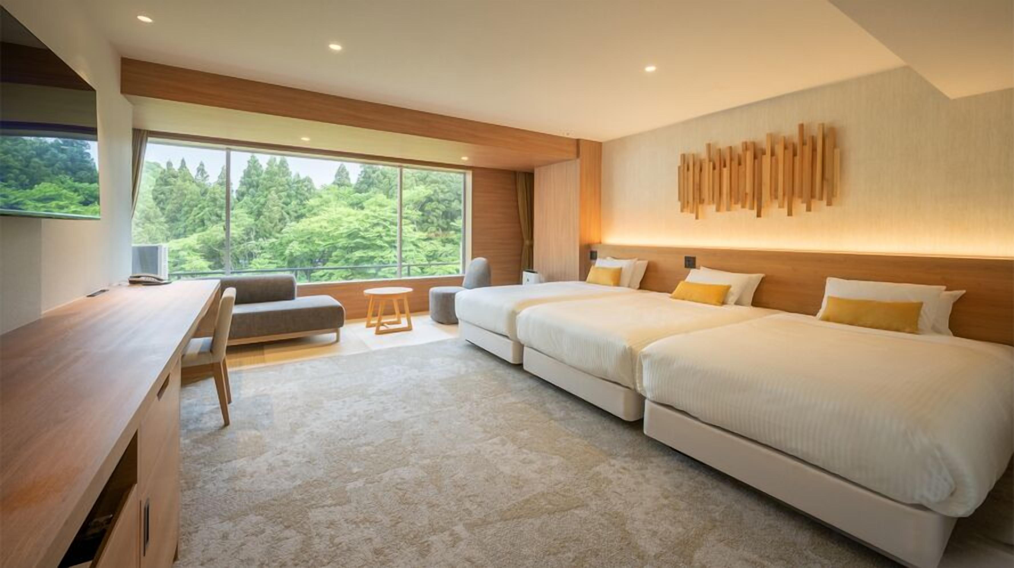 Een moderne hotelkamer met een groot raam, een bureau, een bank en twee bedden.